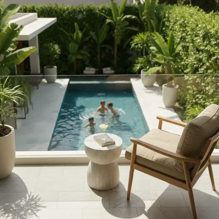 A private suite terrace with a cocktail on a side table, looking down at a secluded swimming pool surrounded by lush gardens.
